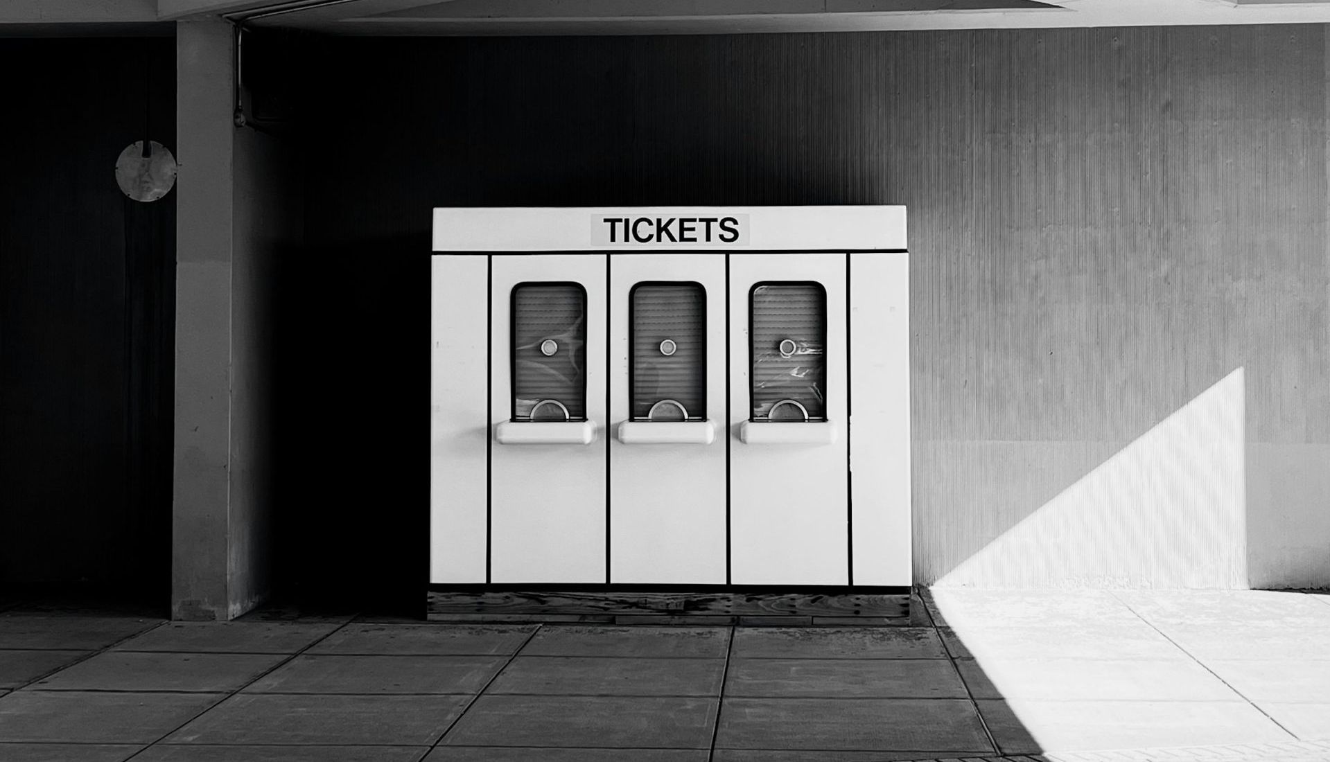 Ein weißer Ticket-Automat mit der Aufschrift TICKETS in einem Betongang, Schwarzweiß